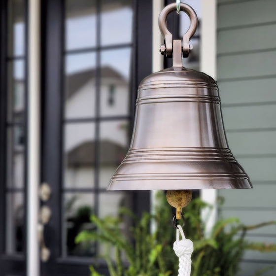 12 inch diameter antiqued brass finish wall bell with shackle hanging  on front porch of home