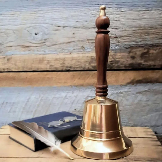 13 inch tall, 6 inch diameter polished brass hand bell with wood handle displayed with a feather pen, book and glasses