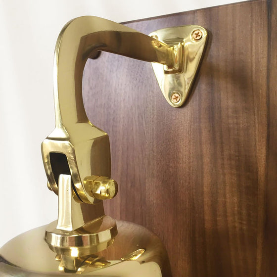 Closeup of three point mounting system on a polished brass wall bell mounted on a walnut plaque