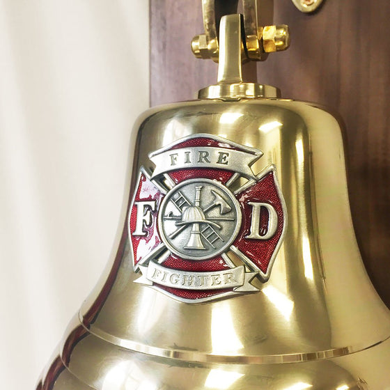 Closeup of red and silver Maltese Cross Fire Fighter medallion mounted on the face of a polished brass bell