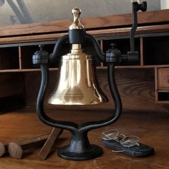 Medium polished finish brass railroad bell with no engraving shown with railroad spikes and glasses for size reference
