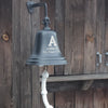 10 inch diameter solid brass wall bell in bronze finish engraved with large letter "A" over family name Abbott and established date shown with weathered wood building in background