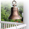 18 inch diameter personalized antiqued finish solid brass bell with round shackle on top hanging from a front porch outside