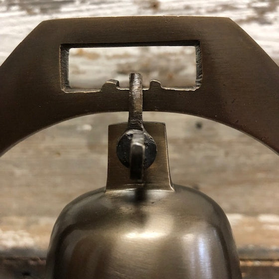 Closeup of how desk bell is attached to brass arch with a shackle, thumb screw combo