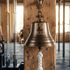 7 inch antiqued finish wall bell mounted on a rough vertical beam in a gym with words PR BELL engraved on the face of the bell