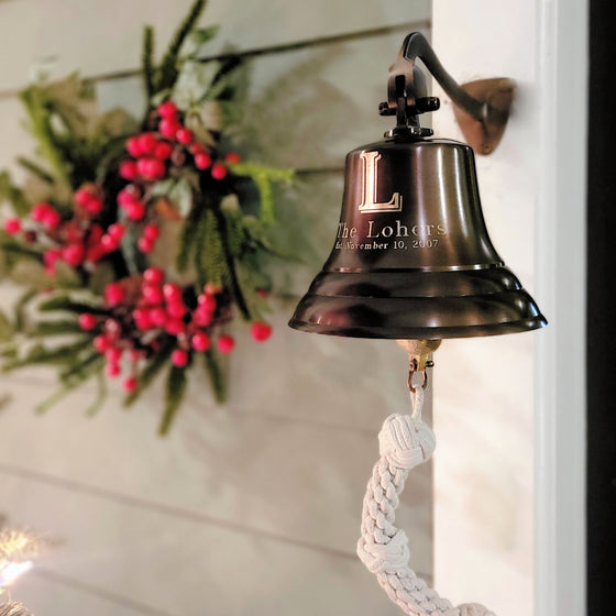 7 inch antiqued brass wall bell with large engraved family initial hung on porch with wreath in background