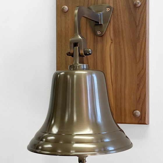 Closeup of 8 inch antiqued brass bell attached to bottom of walnut wood plaque
