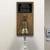 8 inch diameter antiqued brass bell on a walnut plaque with an engraved black plate in a medical office