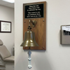 8 inch diameter antiqued brass bell on a walnut plaque with an engraved black plate in a medical office
