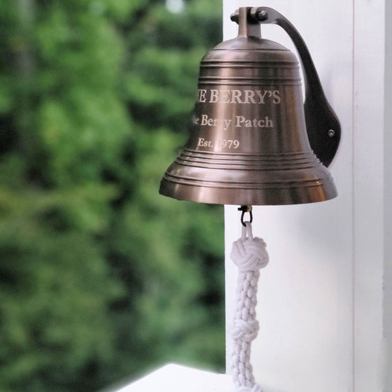 8 Inch diameter antiqued brass wall bell with ridges shown mounted on outside white beam