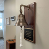 7 inch antiqued brass finish brass wall bell with an engraved business logo mounted on a walnut wood plaque with a black and gold large engraved plate
