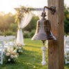Decorative bell with 'Mullins' engraving on a wooden post, outdoor setting with chairs and flowers.