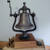 Large dark brown replica railroad bell on a wood base with rail spikes and glasses for size perspective
