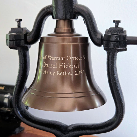 Antiqued brass replica railroad bell with engraved text on a white background