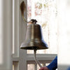 10 inch diameter antiqued brass color bell with ridges in design and a hand ringing bell to show comparative size
