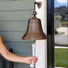 10 Inch distressed finish wall bell hung by front door with hand holding cotton pull rope to show size of bell