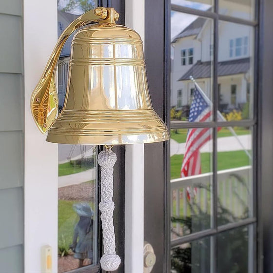 Polished finish 10 inch diameter solid brass bell hung outside near front door with American flag reflected in background