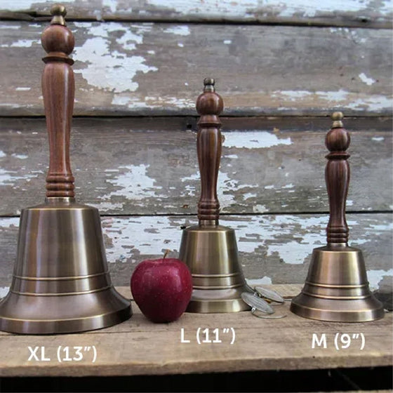 Three antiqued finish hand bells ranging in size from 13 inches high on left, to 11 inches high and 9 inches on right, with an apple for size comparison