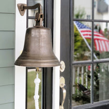  Large 12 inch diameter wall bell with distressed, antiqued brass finish hanging near front door with American flag reflected in background