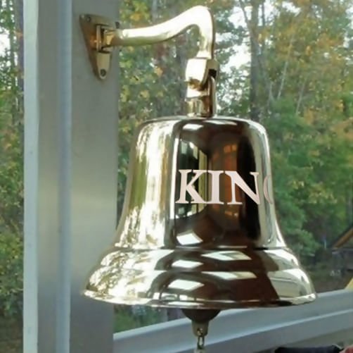 12 inch diameter polished brass finish wall bell with mount hanging on back porch with word "KING" engraved in large letters on front