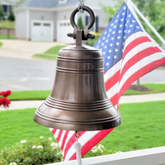 18 inch ridged antiqued solid brass bell with shackle attachment hanging on front porch with American flag in background