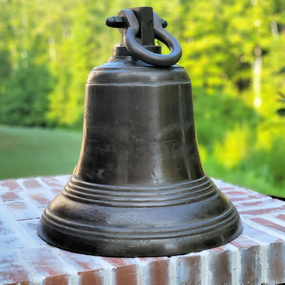 Closeup of  large 18 inch distressed ridged brass bell on bricks with trees in background