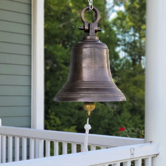 Large 18 inch diameter distressed antiqued finish brass ridged bell hanging on chain from shackle on front porch