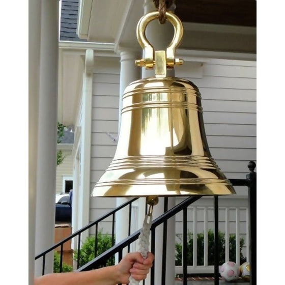 Large 18 inch polished brass ridged bell hanging from shackle on porch with arm grasping pull rope for size reference
