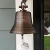 Five inch diameter antiqued brass wall mounted bell with three lines of engraving mounted on house wall