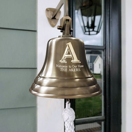 Antiqued finish 7 inch diameter solid brass wall bell with large A and "Welcome to our Home" on one line underneath and THE AKERS below that