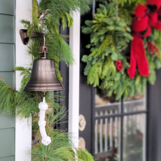 7 inch antiqued brass finish wall bell on front porch near door with Christmas wreath in background