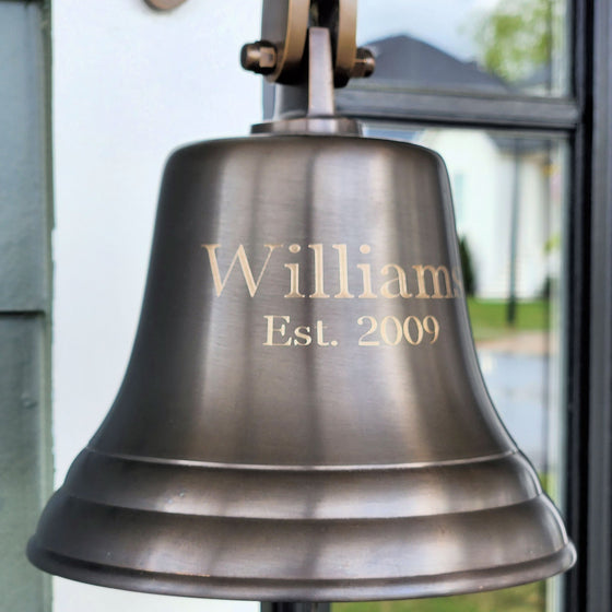 Closeup of personalized custom engraving on the front of a 7 inch diameter antiqued finish solid brass wall bell