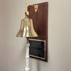 7 inch diameter polished finish solid brass wall bell mounted on a walnut wood plaque with a large black and gold plate with six lines of customized engraving