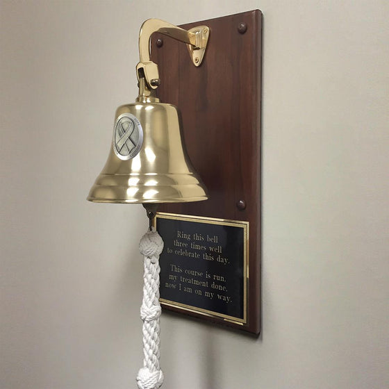 7 inch polished finish solid brass wall bell with large pewter cancer ribbon medallion mounted on walnut plaque with black and gold engraved metal plate about ringing bell when treatment is done
