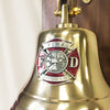 Closeup of red and silver Maltese Cross Fire Fighter medallion mounted on the face of a polished brass bell
