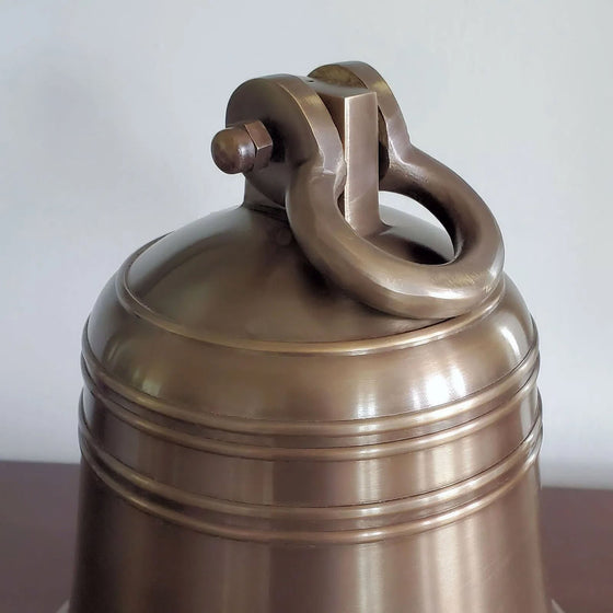 Closeup of round shackle attachment on antiqued brass bell 