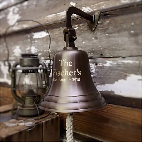 8 inch diameter antiqued finish solid brass wall bell hanging on barn wood wall with three lines of optional engraving