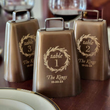  3 large 6.5 inch tall antiqued finish solid brass cow bells engraved with wreath designs, table number and wedding name and date on each one