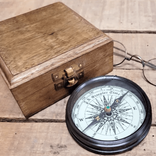 Bottom section of 3 inch antiqued brass compass showing compass rose and needle plus wood display box
